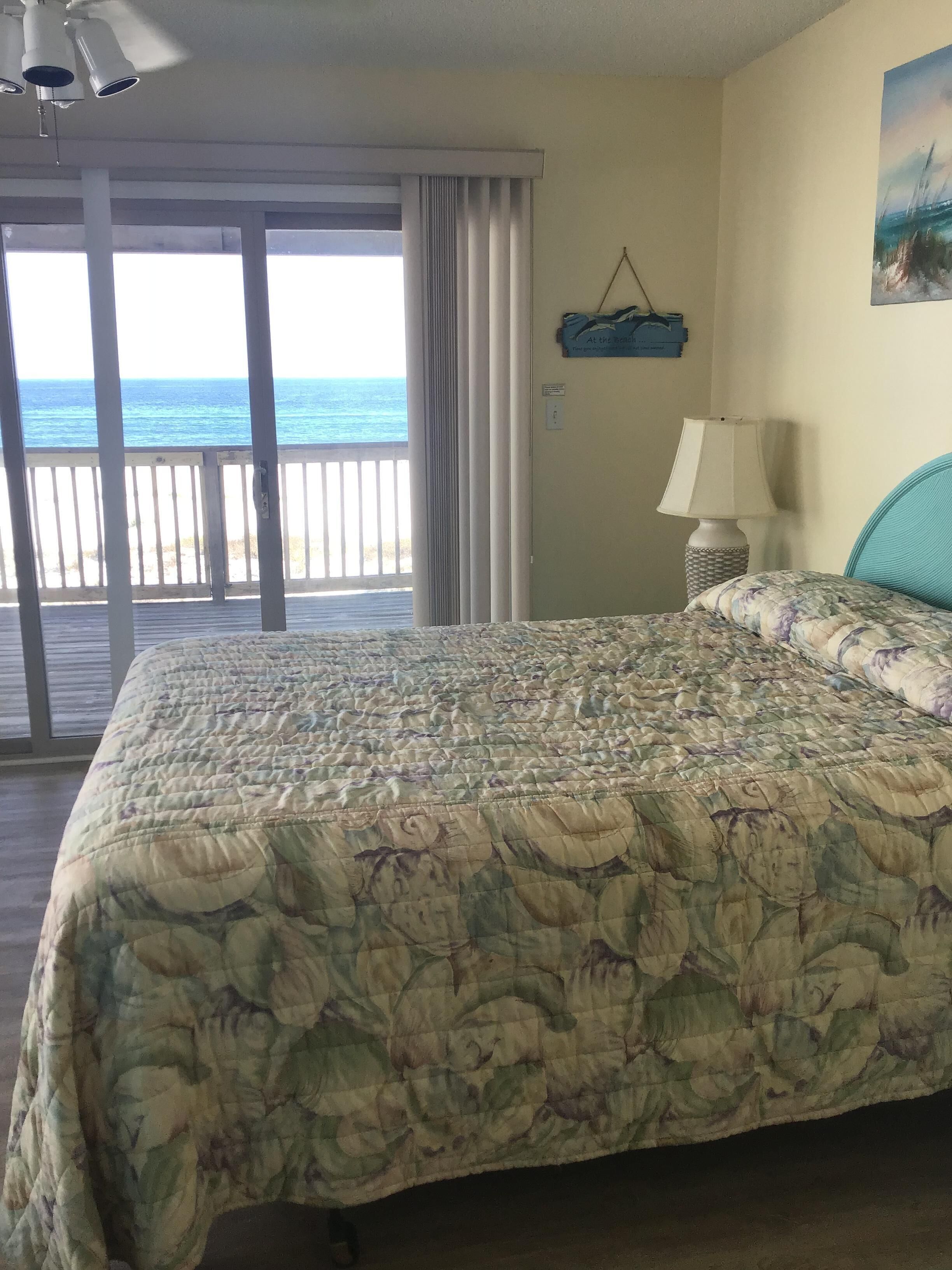 A bedroom with a large bed, a view of the ocean, a lamp, and a painting on the wall.