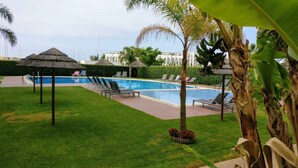 A swimming pool with lounge chairs and a thatched-roof gazebo.