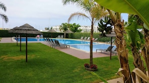 Ein Schwimmbecken mit Liegestühlen und einem Gazebo mit Reetdach.