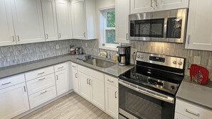 A modern kitchen with white cabinets, a stainless steel microwave, a black stove, and a coffee maker. - Private house with 3 suites. Modern, Clean & Comfortable! (Portland)
