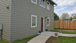A two-story house with a grey siding exterior, a front door, and a small front yard with a concrete pathway and potted plants. - Private house with 3 suites. Modern, Clean & Comfortable! (Portland)