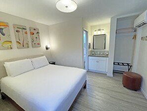 Ein Hotelzimmer mit einem großen Bett, einem Badezimmer mit Spiegel und Waschbecken sowie einem Kunstwerk an der Wand.