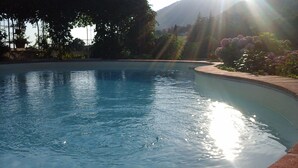 Ein Schwimmbecken mit klarem Wasser, umgeben von einem angelegten Garten und einem Berg im Hintergrund.