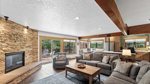 A spacious living room with a stone fireplace, large windows, and a kitchen area. - Private Sunken Outdoor Hot Tub, Near 3 Ski Resorts! (Frisco)