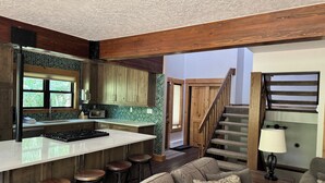 A modern kitchen with a central island, wooden bar stools, and a staircase leading to a loft area. - Private Sunken Outdoor Hot Tub, Near 3 Ski Resorts! (Frisco)