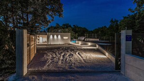A gated entrance to a property with a concrete pathway leading to a building with illuminated walls. - Villa**** SANIVARO with heated pool and SPA (Sanvincenti)