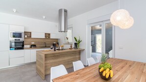 A modern kitchen with white cabinetry, a wooden island, and a dining area with a wooden table and chairs. - Villa**** SANIVARO with heated pool and SPA (Sanvincenti)