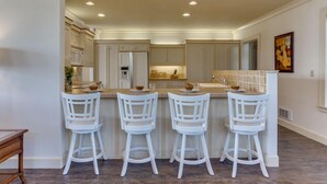 A kitchen with four white bar stools, a central island, and recessed ceiling lights. - Ocean View Home! Hot tub! Dog Friendly! Minutes to the Beach! (Waldport)