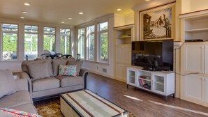 A spacious living room with a sofa, a television, and a bookshelf. - Ocean View Home! Hot tub! Dog Friendly! Minutes to the Beach! (Waldport)
