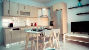 Une cuisine moderne avec des meubles de couleur bois clair, une table à manger avec des chaises, un four encastré et un téléviseur à écran plat posé sur un meuble.