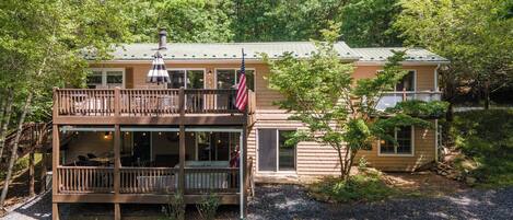 A two-story house with a deck, a flag, and a chimney.