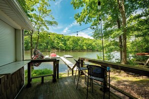 A wooden deck with a table and chairs overlooking a lake, surrounded by trees. - Quiet Lakefront w/ Deck, Dock & Fire Pit (Swanton)