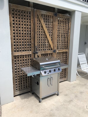 A portable gas grill with four burners, a side shelf, and a storage cabinet, positioned outdoors against a wooden fence. - 2 Rooftop Decks | Downtown IOP | Pool | Elevator | 1 Blk From Beach | Pets (Isle of Palms)