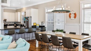 A modern kitchen with white cabinets, a stainless steel refrigerator, and a wooden dining table with chairs. - 2 Rooftop decks, pool/elevator. Downtown IOP, 1 blk from beach. Pet friendly! (Isle of Palms)