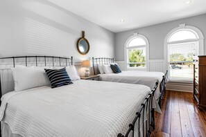 A bedroom with two beds, a mirror, a lamp, and a view of the outdoors through arched windows. - 2 Rooftop Decks | Downtown IOP | Pool | Elevator | 1 Blk From Beach | Pets (Isle of Palms)