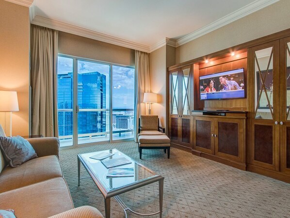 A hotel room with a large window, a television, a sofa, a chair, and a coffee table.