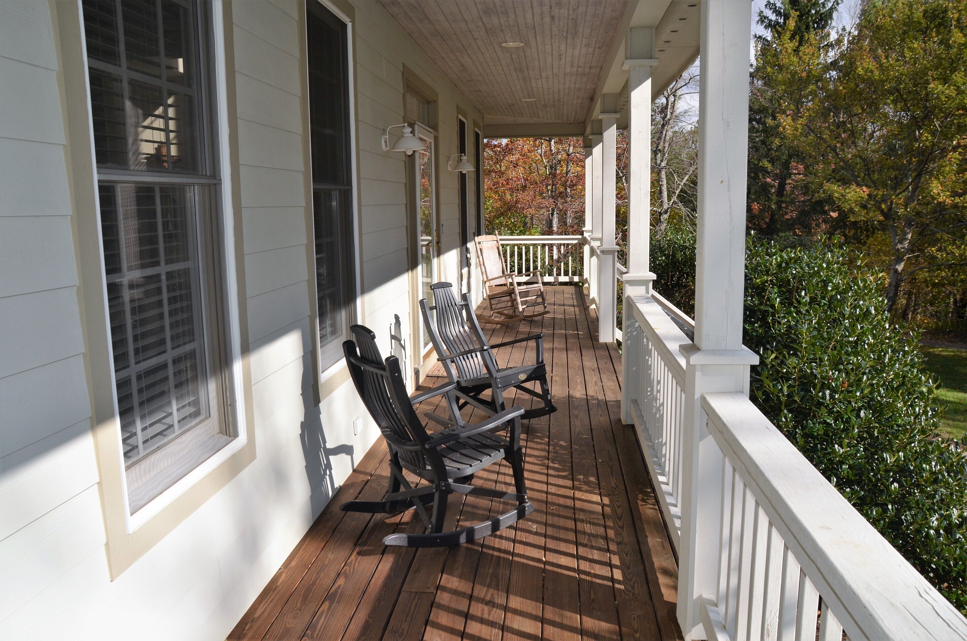 A covered porch with two rocking chairs, a wooden deck, and a white railing.