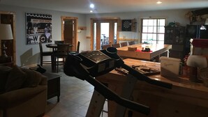 Ein Wohnzimmer mit Laufband, ein Essbereich mit Holztisch und eine Küchenzeile mit Kühlschrank und Schränken.
