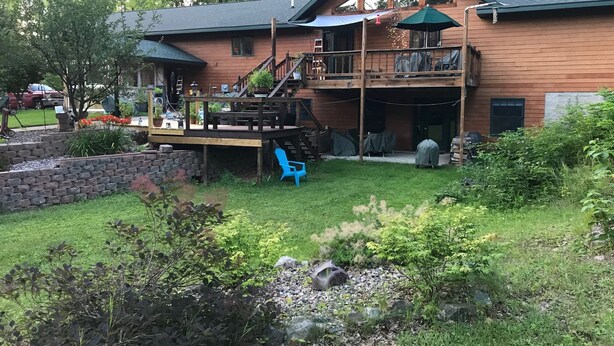 Ein zweigeschossiges Holzhaus mit einer Terrasse, Sitzgelegenheiten im Freien und einer überdachten Veranda.