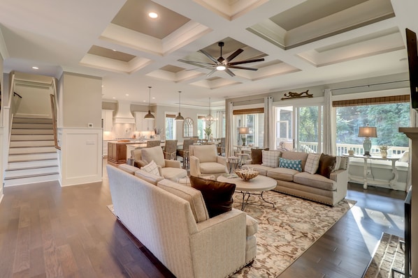 A spacious living room with a large sofa, a coffee table, and a dining area with chairs. There is a staircase leading to another level.