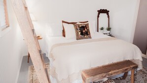 Ein Schlafzimmer mit einem großen Bett, einer hölzernen Bank, einem Spiegel und einem kleinen Tisch mit Pflanzen.