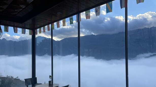 A restaurant with large windows overlooking a mountainous landscape and a cloud-covered valley. - Sapa Valley View Hotel (Sa Pa)