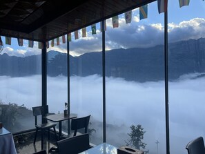 A restaurant with large windows overlooking a mountainous landscape and a cloud-covered valley. - Sapa Valley View Hotel (Sa Pa)