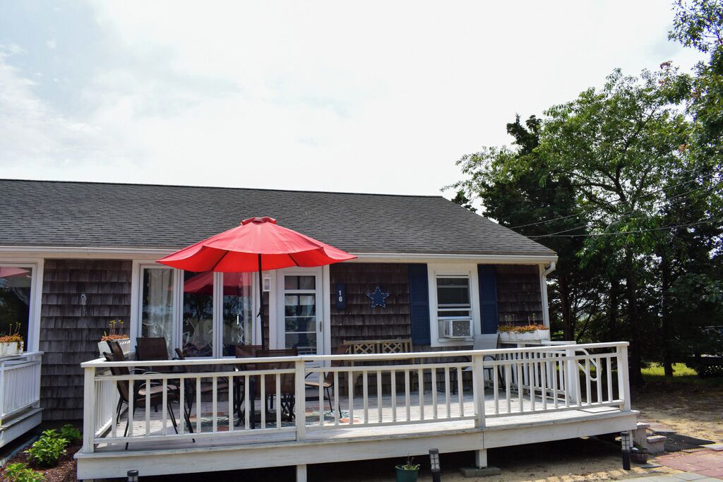 A house with a covered porch, a red umbrella, and a white railing.