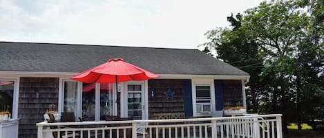 A house with a covered porch, a red umbrella, and a white railing.