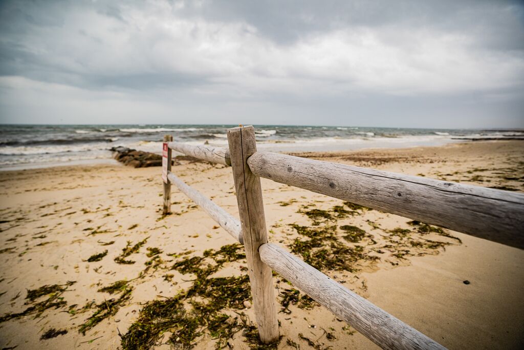 A wooden fence on a beach with seaweed on the sand and a cloudy sky.