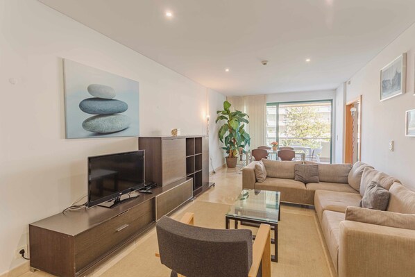 Una sala de estar moderna con un televisor de pantalla plana, un sofá, una mesa de centro de vidrio y una planta grande en maceta.