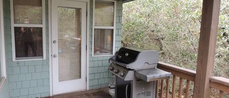 A covered porch with a grill, wooden deck, and a view of trees.