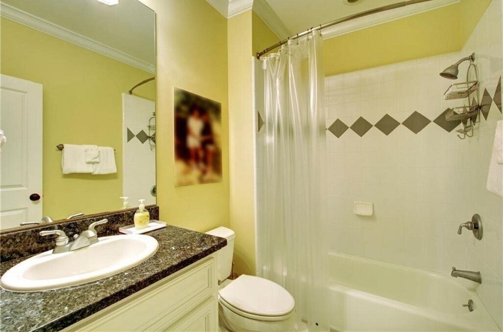 A bathroom with a granite countertop sink, a white toilet, and a glass shower enclosure.