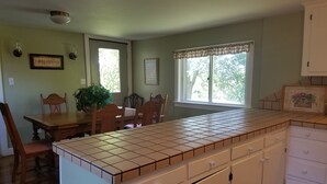 Una cocina con encimera de azulejos, sillas de madera, una mesa de comedor y armarios.