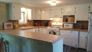 Una cocina con armarios blancos, salpicadero de azulejos, estufa a gas, microondas y refrigerador.