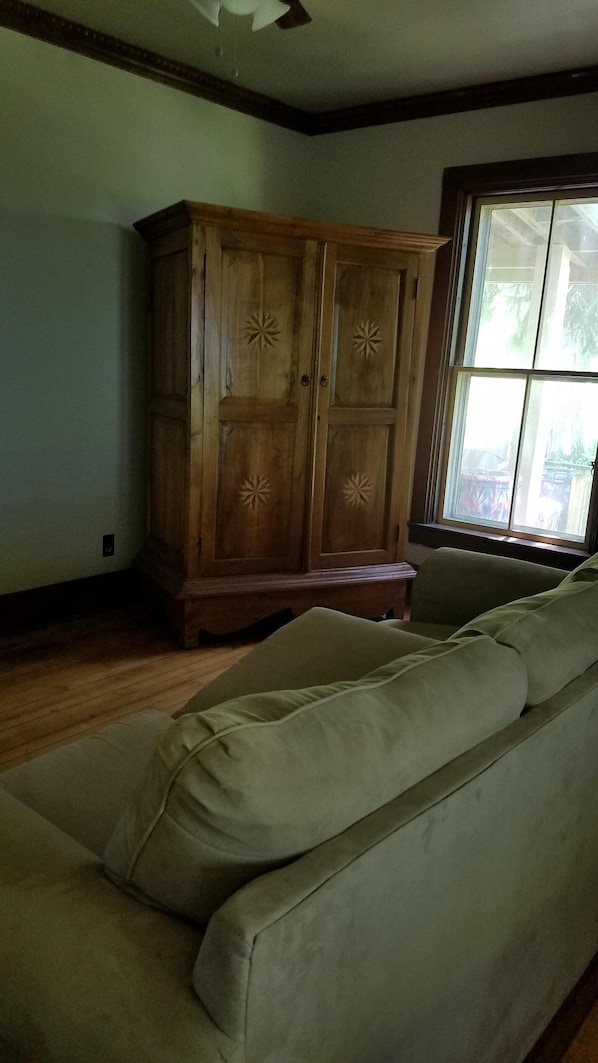 Una habitación con un armario de madera, un sofá color beige y una ventana con vista a árboles.