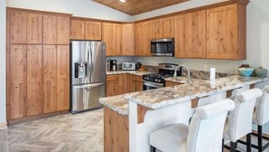 A kitchen with wooden cabinets, stainless steel appliances, a granite countertop, and a bar area with chairs. - Deck, Bikes, Newer Build in Upper Kings Beach (Kings Beach)