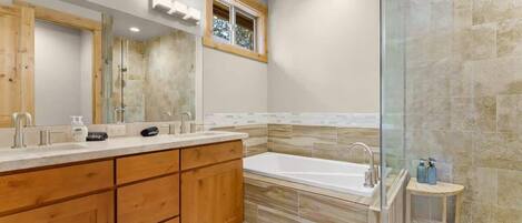 A modern bathroom with a large mirror, wooden vanity, a bathtub, and a glass shower enclosure.