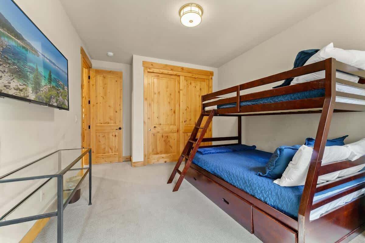 A bunk bed room with a wooden ladder, a desk with a glass top, and a painting on the wall.