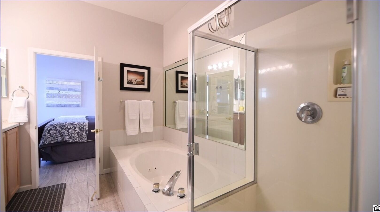 A modern bathroom with a glass-enclosed shower, a bathtub, and a toilet. There are towels hanging on the wall and a small shelf with toiletries.