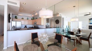 Cozinha moderna com ilha central, área de jantar com mesa de vidro e sala de estar com sofá e televisão.