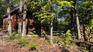 A cabin surrounded by trees, with a wooden deck and a picnic table. - Grandpa's cabin nestled in a little woodland village - playground & pond access (Winslow)