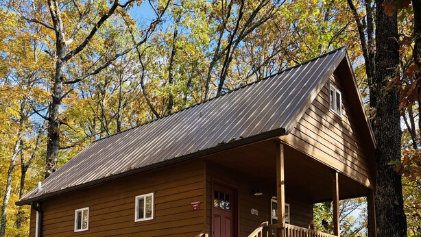 A wooden cabin with a porch, a staircase, and a gravel driveway. - Grandpa's cabin nestled in a little woodland village - playground & pond access (Winslow)
