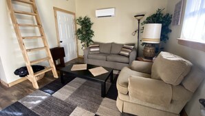 A living room with a sofa, armchair, coffee table, and a wooden ladder. - Grandpa's cabin nestled in a little woodland village - playground & pond access (Winslow)