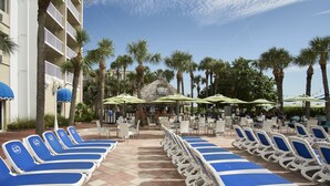 A poolside area with lounge chairs and umbrellas, palm trees, and a building with balconies. - St Pete Beach | Couples Gulf Coast Retreat | Pool + Beach (St. Pete Beach)