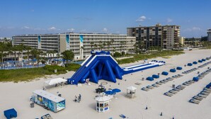 A beachside hotel with a large water slide, beach umbrellas, and a beach bar area. - St Pete Beach | Couples Gulf Coast Retreat | Pool + Beach (St. Pete Beach)