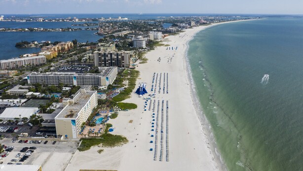 A coastal cityscape with a wide beach, hotel buildings, and a clear view of the ocean. - St Pete Beach | Couples Gulf Coast Retreat | Pool + Beach (St. Pete Beach)