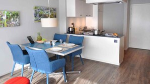 Une cuisine moderne avec des meubles blancs, un coin repas avec des chaises bleues et un petit îlot central doté d’un évier.
