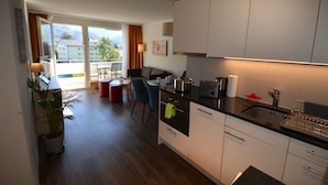 Une cuisine moderne avec des meubles blancs, un plan de travail noir et une vue sur l’extérieur grâce à de grandes portes-fenêtres coulissantes.