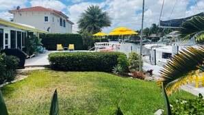 A pool area with yellow umbrellas, a white building with a red roof, and boats docked nearby. - Bright Spacious 3bed/2bath Intracoastal Home (Deerfield Beach)